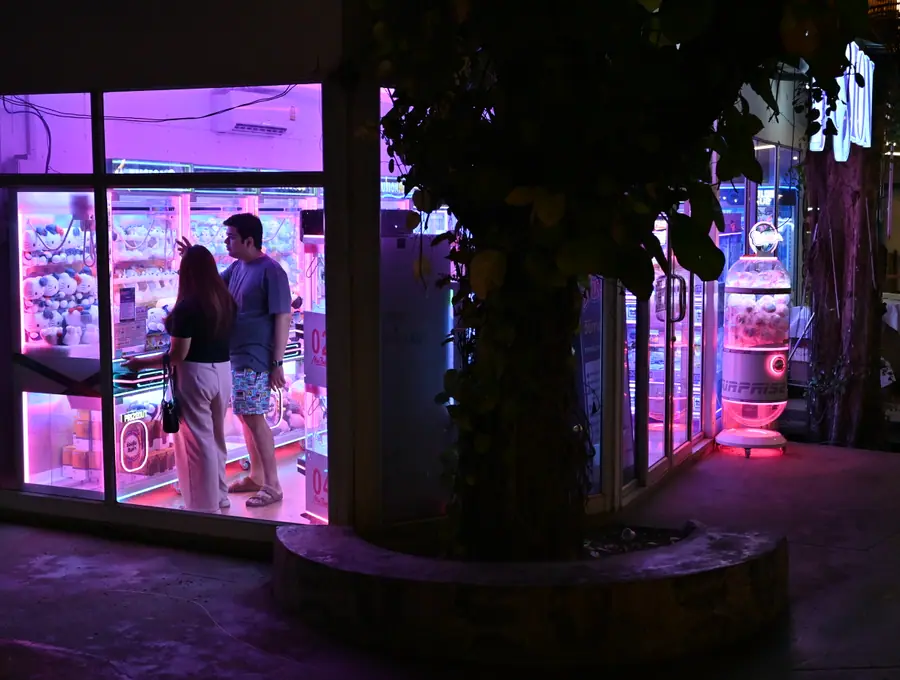 Duas pessoas dentro de um pequeno salão de arcada iluminado a néon